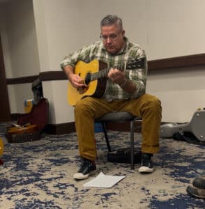Kenny Smith playing a guitar in a hotel conference room