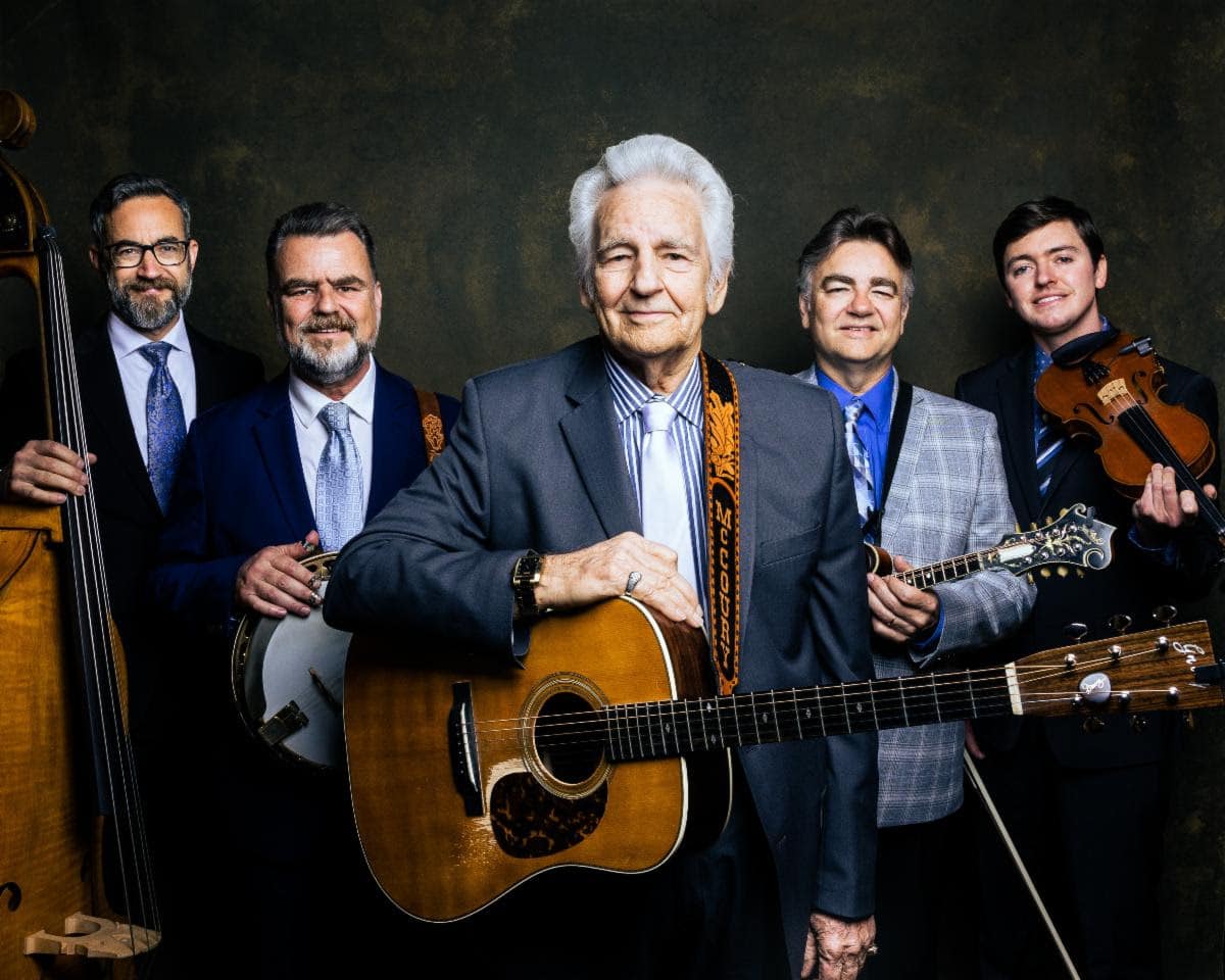 band portrait with Del McCoury in the center with his guitar. Band members are around him with instruments and smiling.