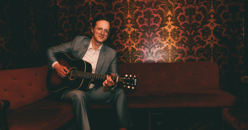 photo of Michael Daves in a suit, playing a guitar sitting down