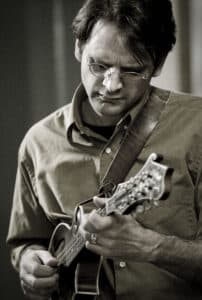 Man playing a mandolin with an intense expression on his face.