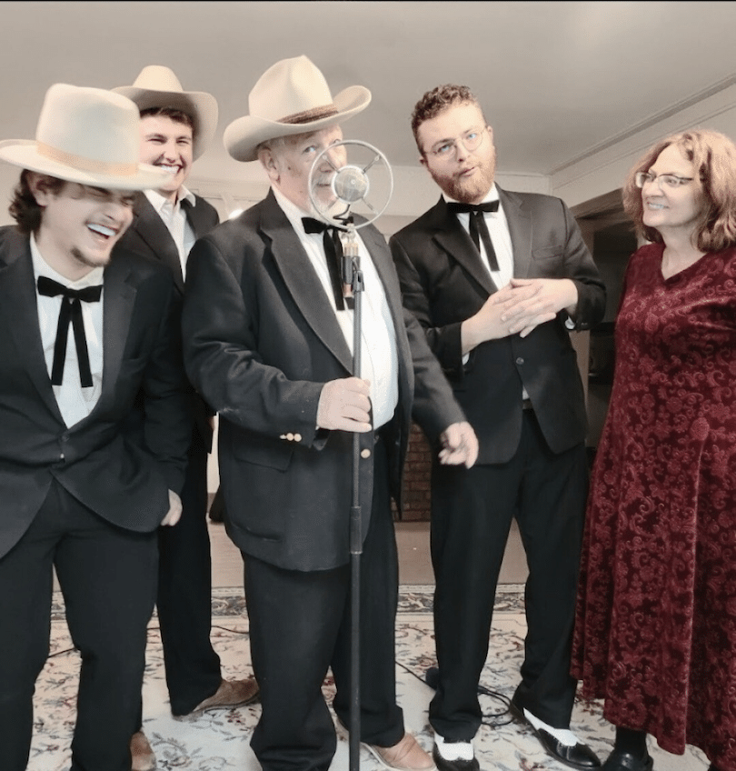 Band photo wearing suits and western hats, string ties. in front of an old fashioned microphone.