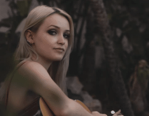 a woman playing guitar and looking at the camera.