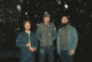 3 men in what looks to be a snow storm, smiling at the camera. The band Hound & Handler.
